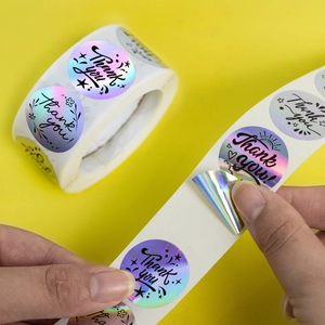 Close-up of peeling a holographic laser Thank You sticker from the roll for packaging