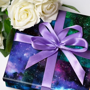 Detail of a gift box wrapped in purple galaxy paper with a satin ribbon and bow