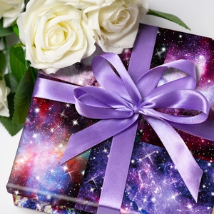 Détail du papier de scrapbooking galaxie rose emballant une boîte avec nœud satin