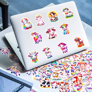 Rainbow cow cartoon stickers decorating a laptop and scattered on a desk