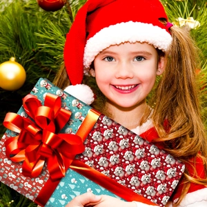 Fille tenant un grand cadeau de Noël avec papier motif chiot et nœud en soie rouge