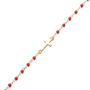 Détail de la chaîne dorée avec perles rouges et pendentif croix poli sur fond miroir