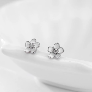 Détail macro de boucles d'oreilles fleurs en argent s925 avec émail blanc et zircons