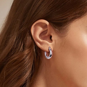 Gros plan d'une boucle d'oreille créole argentée polie portée par un mannequin