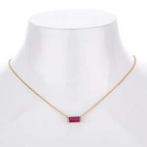 Detail showing a gold necklace with a rectangular pink stone on a white neck model