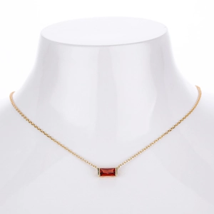 Detailed close-up of a gold necklace with a rectangular red zircon pendant on a mannequin