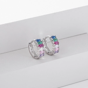Macro shot of silver huggie earrings with marquise-cut colorful gemstones on white stand