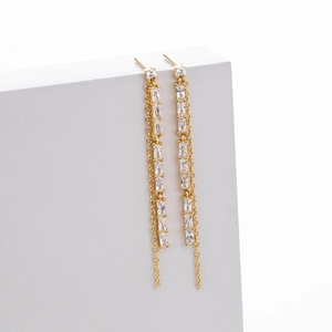 Detalle macro de pendientes dorados con borlas y piedras de corte baguette y cadenas