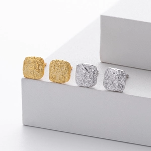 Detail van vierkante lava textuur oorbellen in goud en zilver op witte geometrische stands