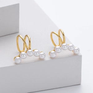 Macro detail of gold ear cuff featuring five white pearls on a minimalist display