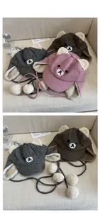 Detailed close-up of plush bear ear hats in pink, grey and brown with pom-pom ties
