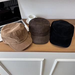 Three suede flat top cadet caps in khaki, brown, and black colors on a wooden desk