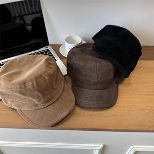 Three suede flat top cadet hats in khaki, brown and black colors on wooden desk