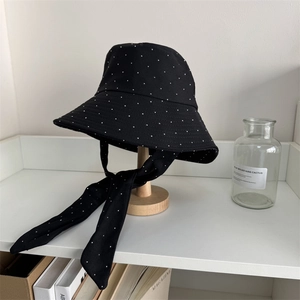 Breathable black polka dot bucket hat with long ribbons on a wooden display stand