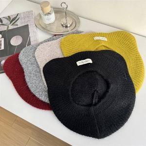 Boina clásica de punto de lana para mujer en cinco colores sobre una mesa blanca
