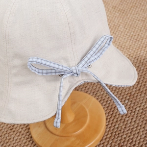 Close-up of beige cotton linen sun hat featuring a blue plaid bow on a wooden stand