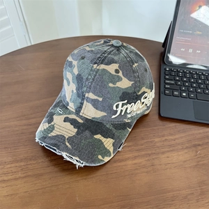 Distressed camo baseball cap with vintage embroidery and ripped brim on wooden table