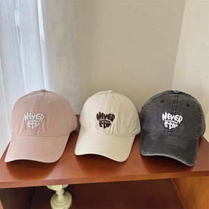 Embroidered cotton baseball caps in pink, beige, and charcoal grey on a display stand