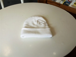 Detail van een witte gebreide muts met stijlvolle zilveren veiligheidsspeldjes