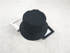 Détail d'un chapeau bob en toile noire avec anneaux métalliques sur un tapis blanc en peluche
