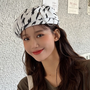 Detail of white cotton beret with black abstract stripes and silver chain accessory