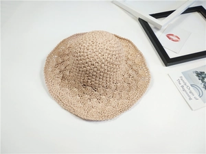 Dettaglio cappello di paglia beige all'uncinetto con bordo ondulato e trama traforata