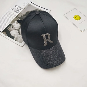 Close-up of a black satin baseball cap featuring a sparkling rhinestone R letter emblem