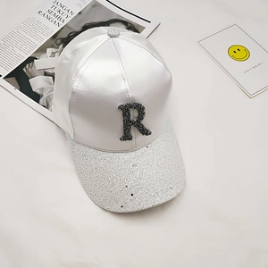 Detailed view of white satin baseball cap with rhinestone letter R and silver glitter brim