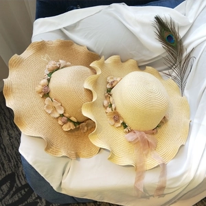 Women's beige straw sun hat with floral wreath and wavy brim for beach vacation