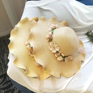 Detail of woven straw hats featuring floral garlands and elegant ribbon ties on white fabric