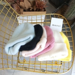 Knitted Angora rabbit fur beanies in six colors arranged on a golden chair