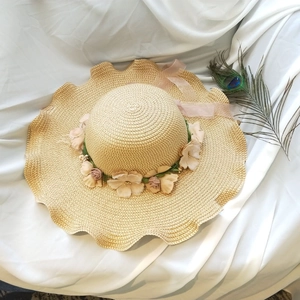 Close-up of khaki straw hat with floral wreath and pink chiffon ribbon on white silk