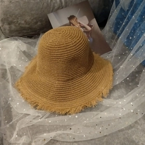 Detail shot of camel straw bucket hat featuring raw fringe edges on a soft fabric sofa