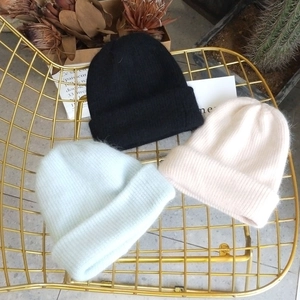 Close-up of thick angora wool hats in black, cream, and teal on a stylish metal chair