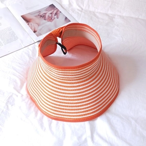 Detail of orange and white striped straw sun hat with adjustable strap on white fabric
