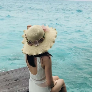 Women's beige straw sun hat with floral wreath and wavy brim for beach vacation