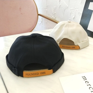 Detalle de la correa de cuero ajustable con 'FOUNDED 1986' en gorros negro y beige