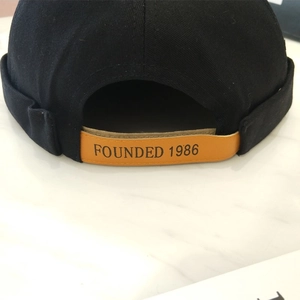 Detalle de gorra docker negra con correa de cuero y texto 1986 grabado en la parte posterior
