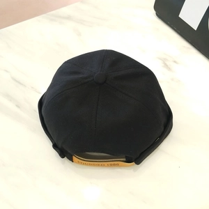 Detalle de la gorra docker de lona negra con correa de cuero y relieve de 1986