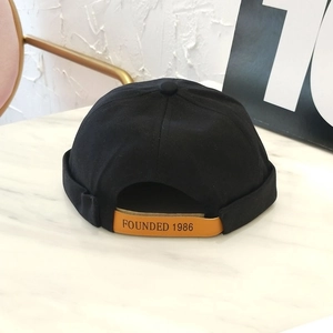 Detalle de gorro docker de algodón negro con correa de cuero y texto Founded 1986