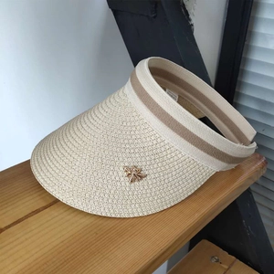 Detail of beige straw sun hat featuring a striped band and small gold bee metal ornament