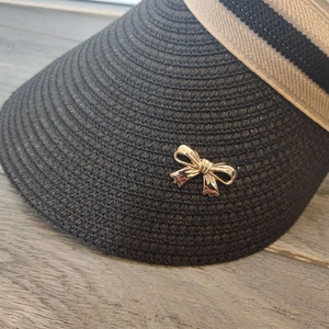 Close-up of black woven straw sun hat with a decorative gold metal bow detail
