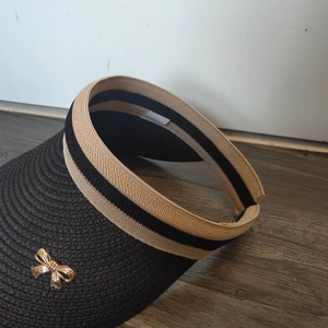 Detail of black woven sun visor with striped band and golden metal bow decoration