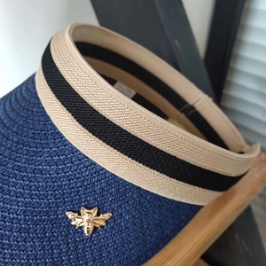 Close-up of navy straw sun visor with golden bee emblem and striped headband detail