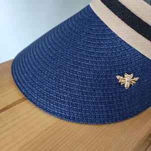 Detail of blue straw sun hat with gold bee emblem and striped ribbon trim