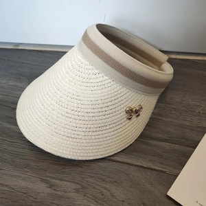 Detail of white straw sun visor featuring a gold bow buckle and striped ribbon band