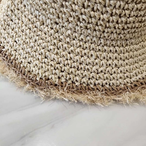 Close-up of dual-tone raffia woven sun hat with natural raw fringe and handmade texture