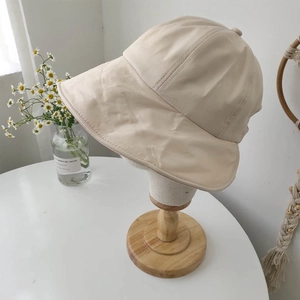 Detail view of foldable cream bucket hat with wide brim on a display stand