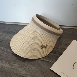 Detail of straw sun visor with striped elastic band and gold bow buckle on wood surface