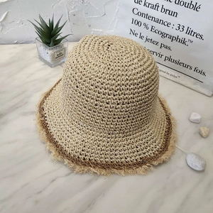 Detailed close-up of handmade beige straw bucket hat with frayed edges and brown trim